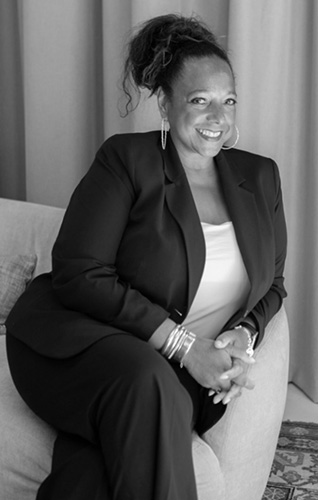 Vrouw in een blazer zittend op een bank met een zelfverzekerde glimlach - Gissella