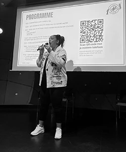Vrouw zingt op podium met presentatie achter zich